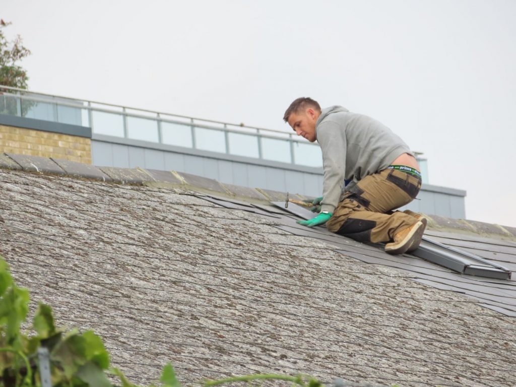 handyman putting roof tiles on roof